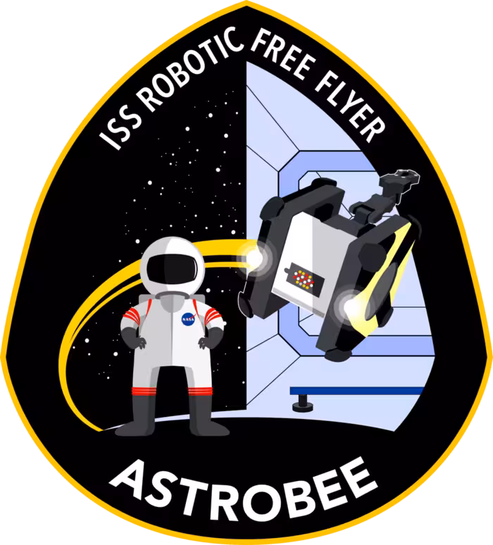 Astrobee mission patch. A teardrop shaped yellow bordered emblem with the words ISS ROBOTIC FREE FLYER arching across the top, an astronaut in a white spacesuit on the left, a cube shaped Astrobee robot with yellow propulsion exhaust on the right in front of a stylised cupola window, and the word ASTROBEE in bold along the bottom